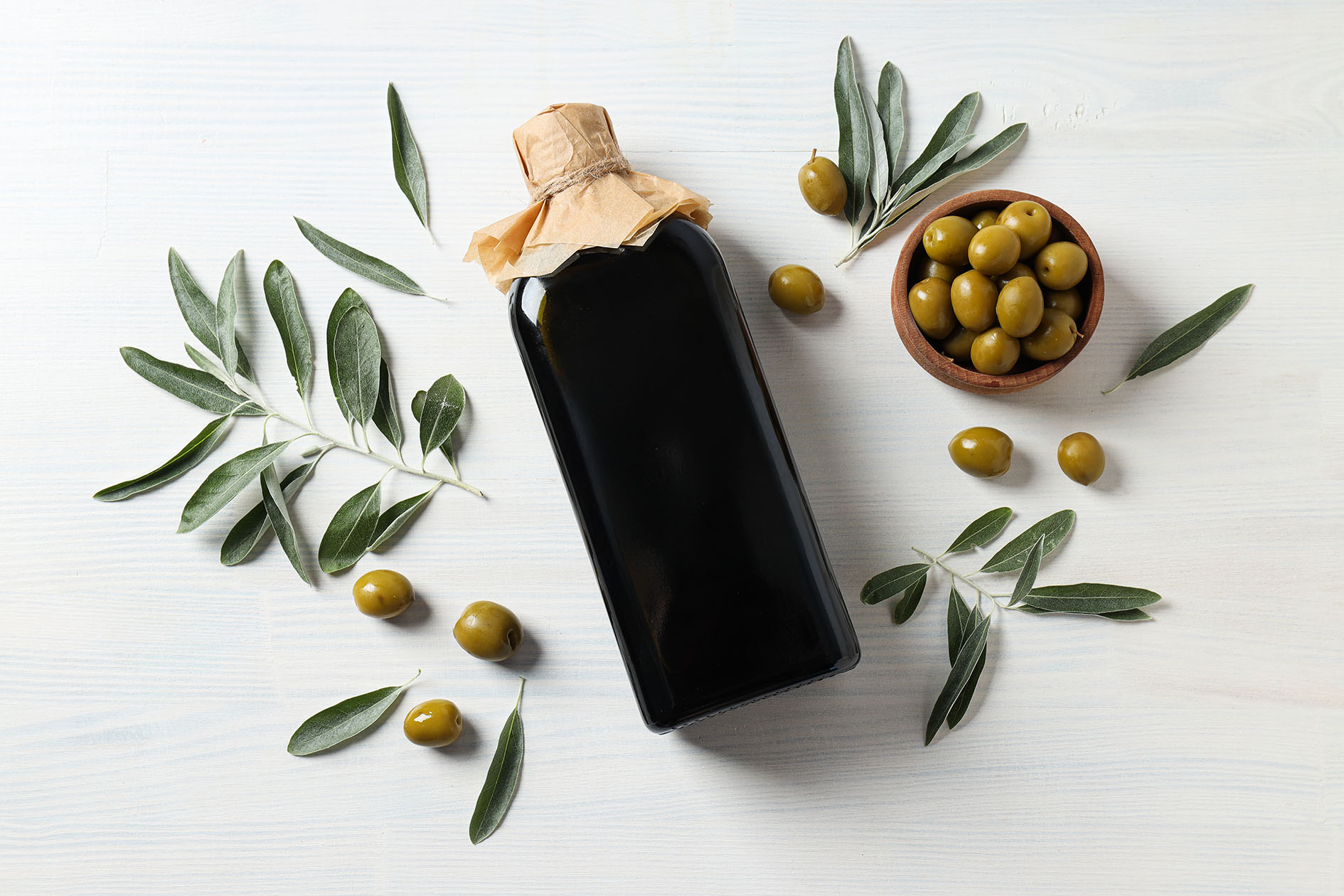 Olive oil bottle and olives on white wooden background, top view